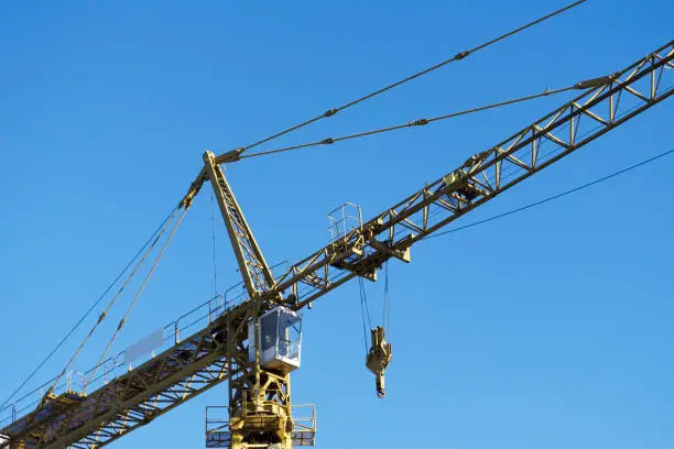 Tower crane yellow close up of cabin and lifting hook high in blue sky uk