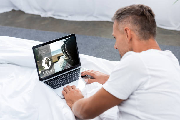 istock man in white t-shirt using laptop with booking website on bed 1060366074