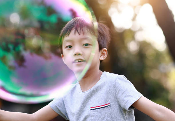 公園でシャボン玉で遊ぶ陽気な幼児の少年 - bubble wand child blowing asian ethnicity ストックフォトと画像