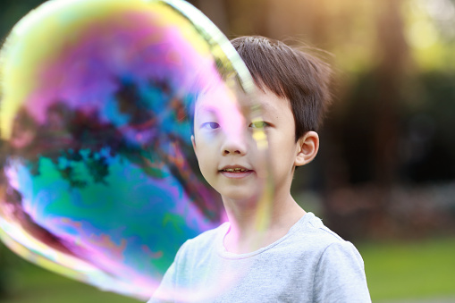 Cheerful toddler boy playing with soap bubbles in park