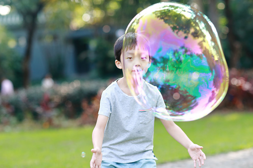 Cheerful toddler boy playing with soap bubbles in park