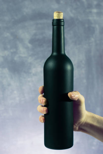 Hand hold Black bottle of red wine on a beautiful  background.