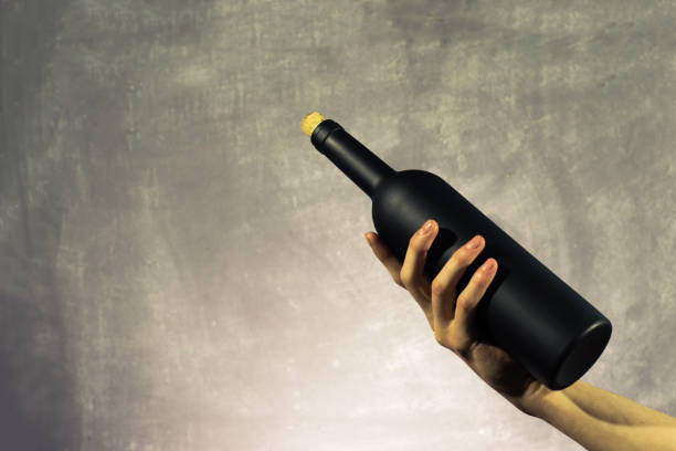 Hand hold Black bottle of red wine on a beautiful  background.