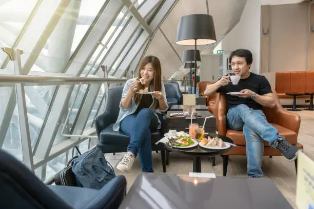 Photo of Asian couple sitting and eatting inn airport lounge when waiting the flight at modern international airport, travel and transportation concept
