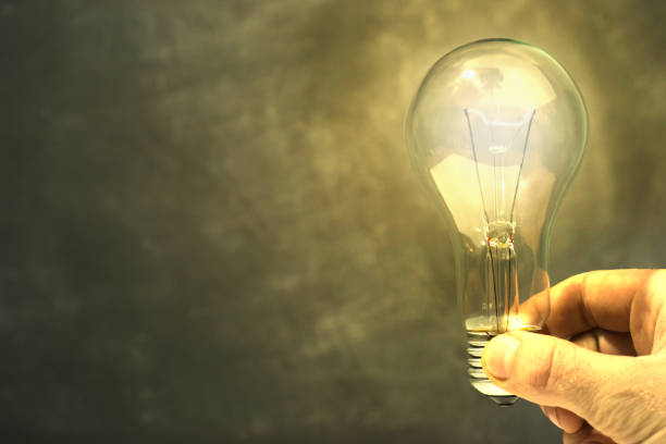 istock Hand holding light bulb in fingers with blackboard behind. Concept and idea background. 1060391082