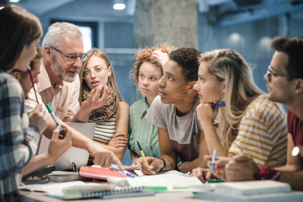 Mature teacher teaching group of college students at campus.