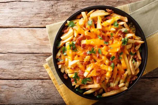 Photo of Freshly cooked French fries baked with cheddar cheese, bacon and parsley closeup. horizontal top view