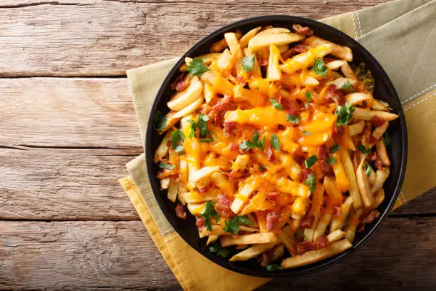 Freshly cooked French fries baked with cheddar cheese, bacon and parsley closeup on a plate. horizontal top view from above