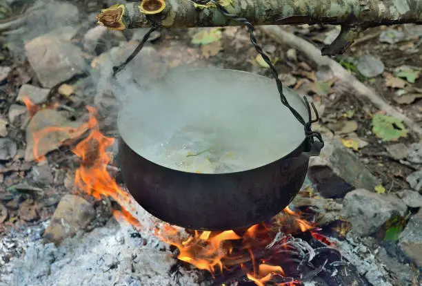 A cooking fish-soup in pot on bonfire.