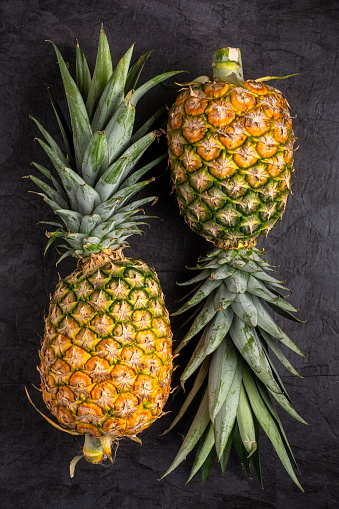 Two Fresh ripe pineapple on dark background, vertical composition , top view