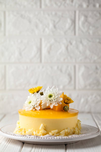 istock Mango cheesecake with yellow jelly topping, with flowers and fresh mango pieces on white background, vertical composition 1060442072