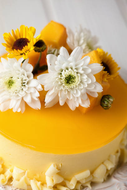 istock Mango cheesecake with yellow jelly topping, with flowers and fresh mango pieces on white background, vertical composition 1060442096
