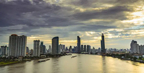 Photo of Cityscape of modern building near the river in the morning with grey and yellow sunrise sky and clouds. Modern architecture office building. Skyscraper with morning sky. Business and finance concept.