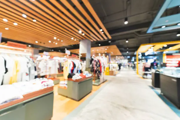Photo of Blurred, defocused background of clothing shops in modern shopping mall or department store. Shopaholic lifestyle, or fashion dress outlet business concept