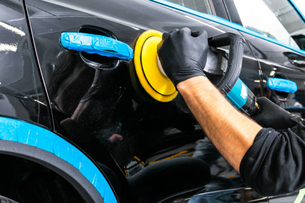 Car polish wax worker hands applying protective tape before polishing. Buffing and polishing car. Car detailing. Man holds a polisher in the hand and polishes the car stock photo