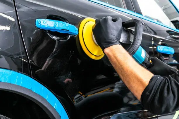 Photo of Car polish wax worker hands applying protective tape before polishing. Buffing and polishing car. Car detailing. Man holds a polisher in the hand and polishes the car