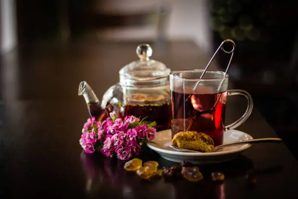 Side view of glass of fruit tea with tea egg decorated with rock sugar, cantuccini, teapot and flowers on wooden table in café