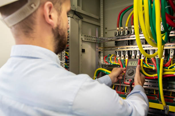 Young electrician measuring voltage in fuse board. Male technician examining fusebox with multimeter probe. Electrician checking voltage in distribution panel. stock photo