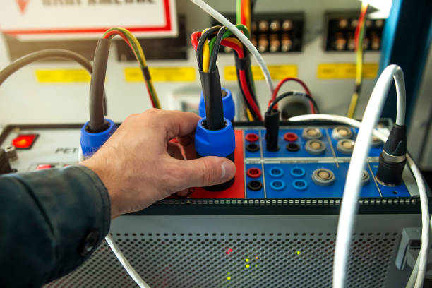 electrician technician engineer with test device for testing relay protections of power high voltage lines, transformers and generators. Maintenance tools. Service man connect plugs to test device ingeniero técnico en electricista con dispositivo de prueba para pruebas de protecciones de transmisión de líneas de alta tensión de alimentación, transformadores y generadores. herramientas de mantenimiento. hombre servicio conectar enchufes para pro