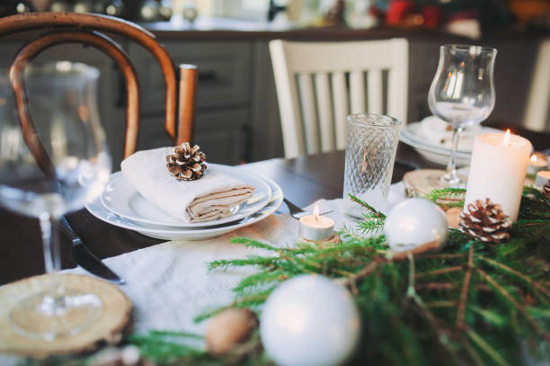 istock Festive Christmas and New Year table setting in scandinavian style with rustic handmade details in natural and white tones. Dining place decorated with pine cones, branches and candles 1060512174