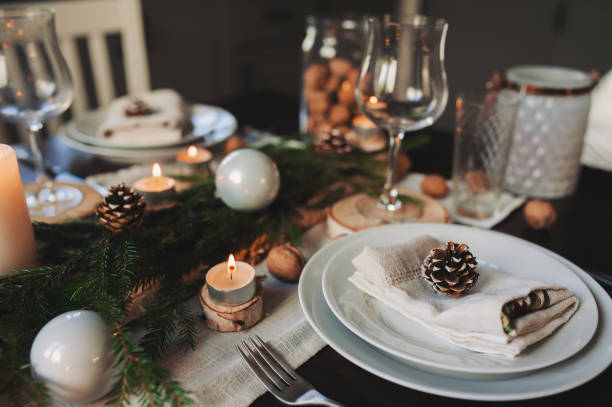 istock Festive Christmas and New Year table setting in scandinavian style with rustic handmade details in natural and white tones. Dining place decorated with pine cones, branches and candles 1060512184