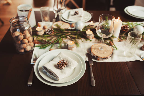 istock Festive Christmas and New Year table setting in scandinavian style with rustic handmade details in natural and white tones. Dining place decorated with pine cones, branches and candles 1060512188