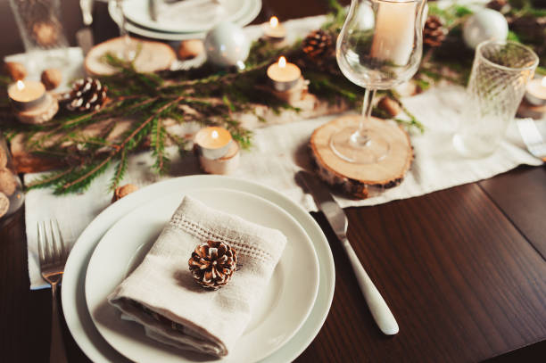 istock Festive Christmas and New Year table setting in scandinavian style with rustic handmade details in natural and white tones. Dining place decorated with pine cones, branches and candles 1060512496