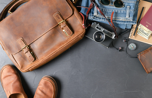 Accessories for travel plan, trip vacation, tourism - vintage bag and leather boot shoe on black stone background. Flat lay and copy space