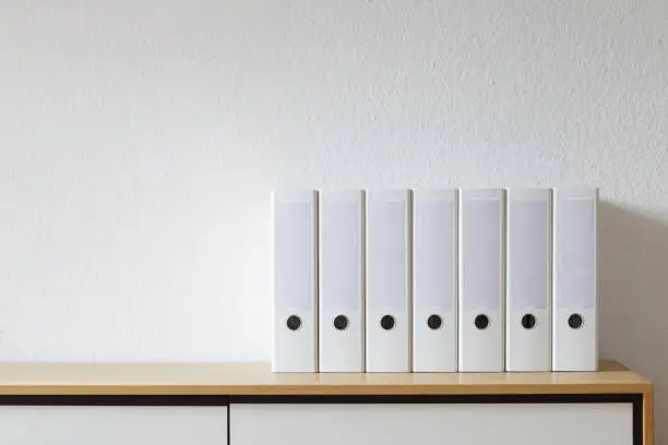 Modern office, white file folders on wooden sideboard in bright office