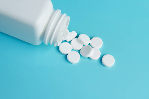 istock Medication bottle and white pills spilled over blue colored background. Medication and prescription pills background. Pharmaceutical drugs. 1060516390