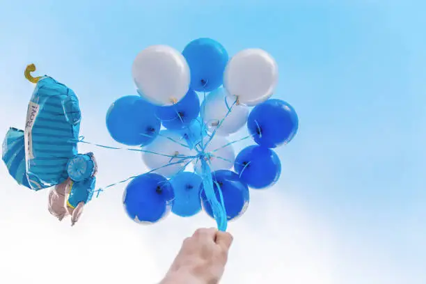 Hand holds balloons blue and white color, against background of sky. Copy space