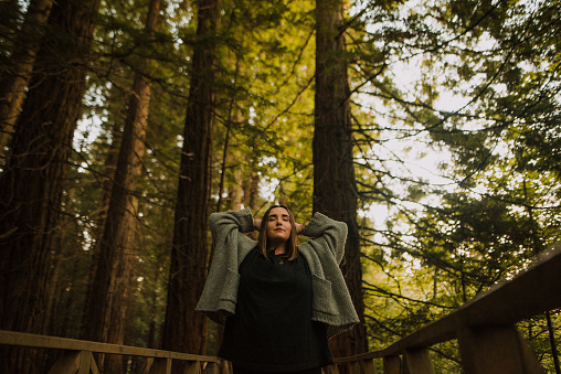 Young woman with hands on head and eyes closed, relaxing inside a beautiful forest