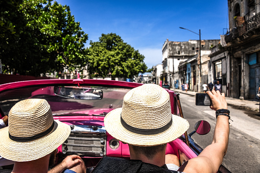 Tourist With Straw Hats Enjoying Cuba In Vintage Car