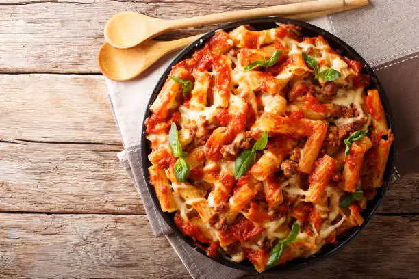 Photo of Pasta ziti with bolognese sauce and cheese close-up. horizontal top view, rustic style