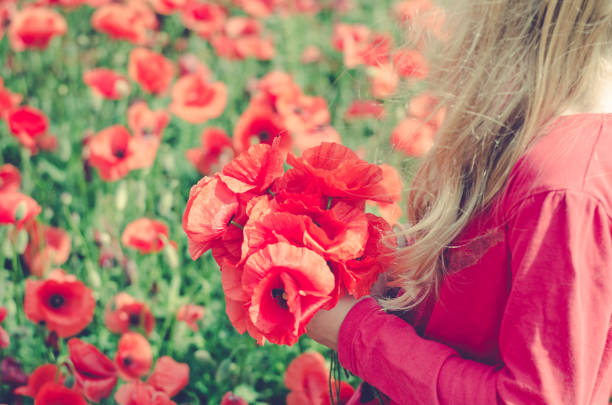 Defocused young beautiful redhead woman in a white shirt with a poppy wreath on her head in a poppy field on sunny summer day