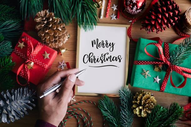 istock Merry christmas concepts with human hand writing cards with gift box present and ornament element on wood table background 1060558594