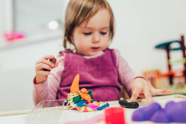 istock Kid girl is playing with plasticine while sitting at table in nursery room 1060562690