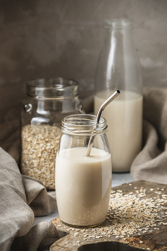 Non dairy oat milk in glass jar with metal reusable drinking straw on rustic background. Oat flakes scattered on the table.