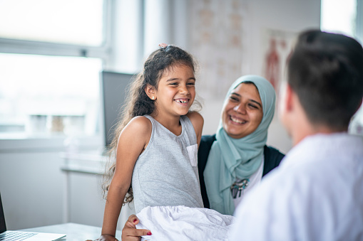 A Muslim mother and daughter are visiting the doctor. The girl is smiling before her checkup.