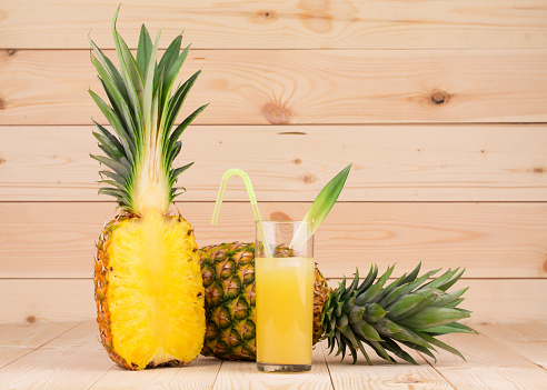 Half of a pineapple and a glass of juice. It is all located on the wooden surface. Close-up.