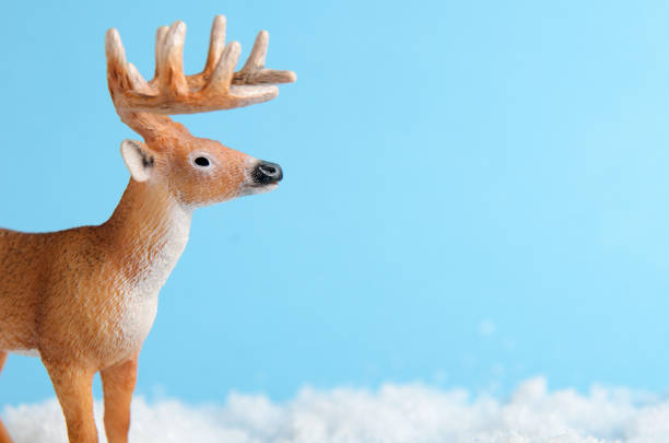 istock Toy deer on blue background is standing on artificial snow close-up. Background for children's or winter advertising banner. Copy space 1060591162
