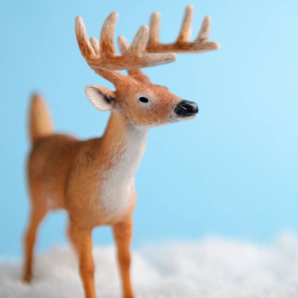 istock Toy deer on blue background is standing on artificial snow close-up. Background for children's or winter advertising banner. 1060591226
