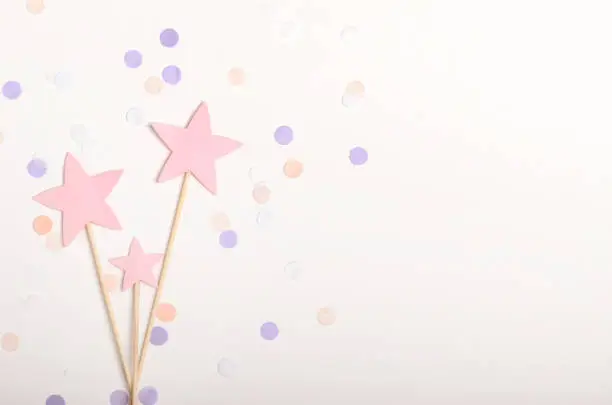 Pink stars on a stick topping on white background with confetti, pastel colors. Children's holiday, new year. Top view, flat lay, copy space.