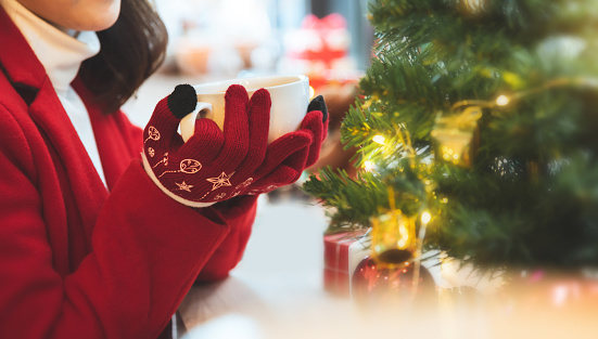 Asian woman in red sweater clothes and gloves holding a cup of coffee in winter day. Copy space. Christmas.