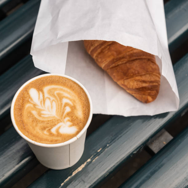 cappuccino café en una taza de papel y un croissant, en banco de madera, al aire libre. - paper glass fotografías e imágenes de stock