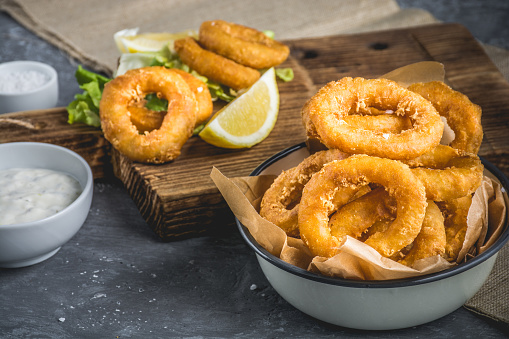 Crispy fried calamari rings with garlic sauce on wooden desk on concrete background.
