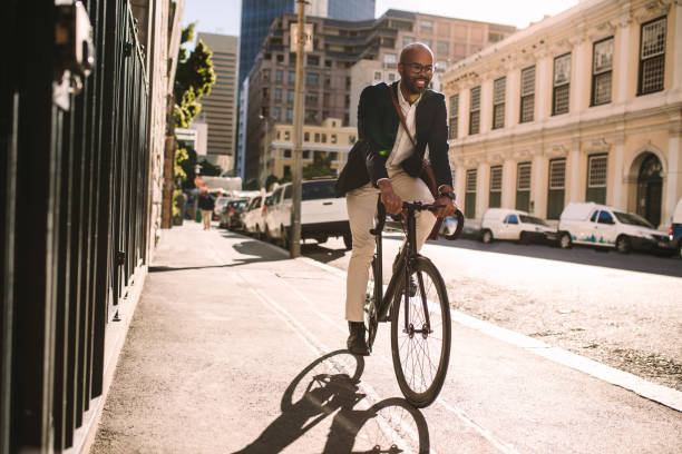 Smiling businessman going to work on bike Young smiling businessman going to work by bike. Man in suit riding bicycle on sidewalk in morning. commuter stock pictures, royalty-free photos & images