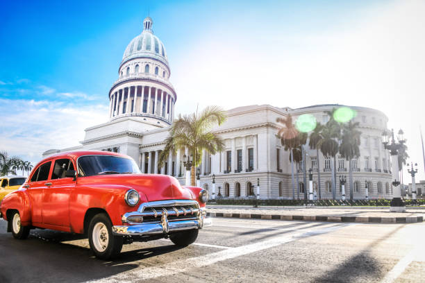 Red Authentic Vintage Car Moving In Front Of El Capitolio Red Authentic Vintage Car Moving In Front Of El Capitolio In Havana, Cuba caribbean sea photos stock pictures, royalty-free photos & images