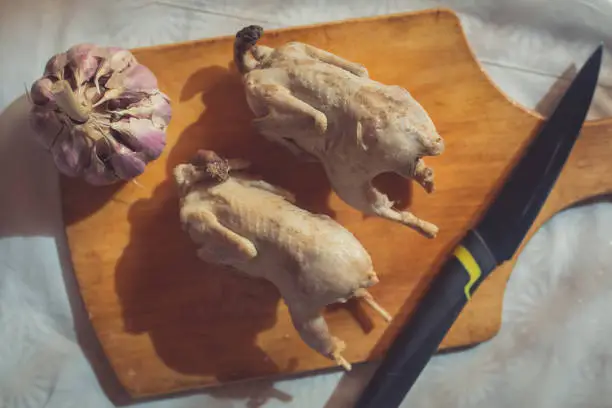 Photo of Two whole cooked quails, garlic and a knife are lie on the cutting board in the kitchen