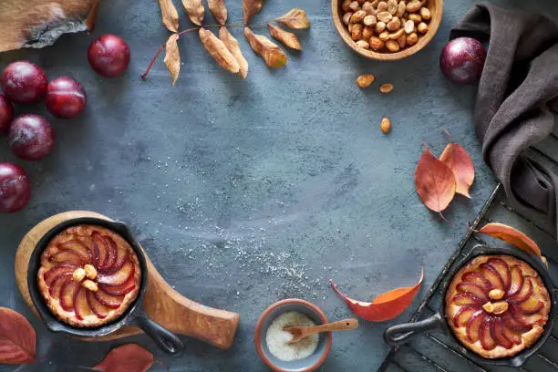 Photo of Cooking background with red plums, plum crumble cakes, towel, caramelized peanuts, autumn leaves, copy-space